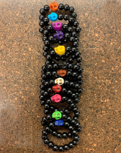 multiple bracelets made with black onyx beads with one colored bead in the shape of a skull