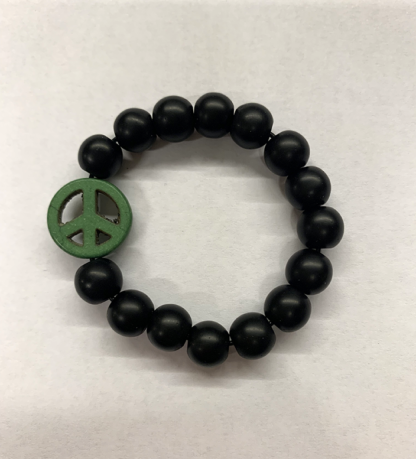 a bracelet made with black onyx beads with one green bead in the shape of a peace sign