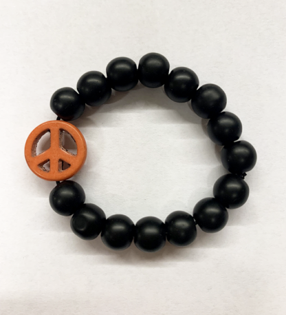 a bracelet made with black onyx beads with one orange bead in the shape of a peace sign