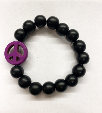 a bracelet made with black onyx beads with one purple bead in the shape of a peace sign