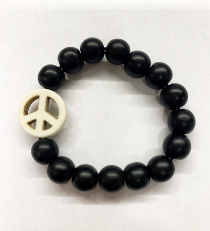 a bracelet made with black onyx beads with one white bead in the shape of a peace sign
